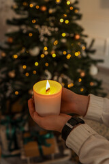 Burning candle in hands on a Christmas tree background