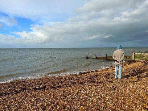 Rear view of a man standing on a beach looking at sea view in autumn, Whitstable, Kent, England, UK