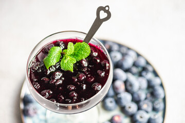 Overhead view of a glass of blueberry jam with mint on a plate with fresh blueberries