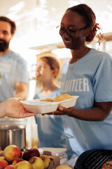 Detailed picture shows volunteers providing free food to the hungry, homeless, and refugees. Close up of female voluntary person distributing meals, providing assistance and sharing non-perishables.