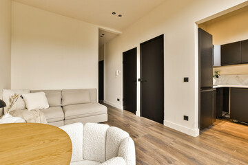 a living room with wood flooring and white walls, there is an open kitchen area in the back wall