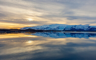 Fototapeta na wymiar Lake and snowy mountains at sunset in iceland with majestic nordic landscape, freezing cold water. Scandinavian roadside scenery with hills during golden hour, wonderland scenic route.