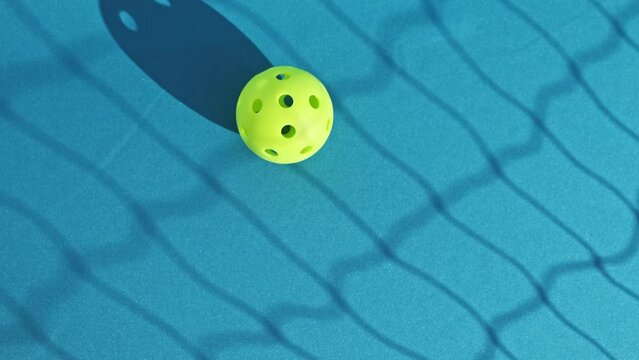 overhead image of a green pickleball being hit by a yellow one on a blue floor with the shadow of the net cast