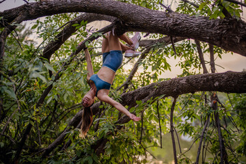 Naklejka na ściany i meble Fit girl with athletic body shape exercises outdoors. She climbs trees, showcasing strength and flexibility. Enjoying a green park environment, she prepares and warms up for training.