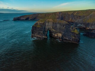 Drone shot of naturally formatted rocky cliffs in the sea under blue cloudy sky at sunset