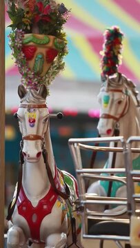 vertical video, beautiful metallic horse of a carnival game carousel, painted in pastel colors in front of a blurred background of colorful blinking light bulbs