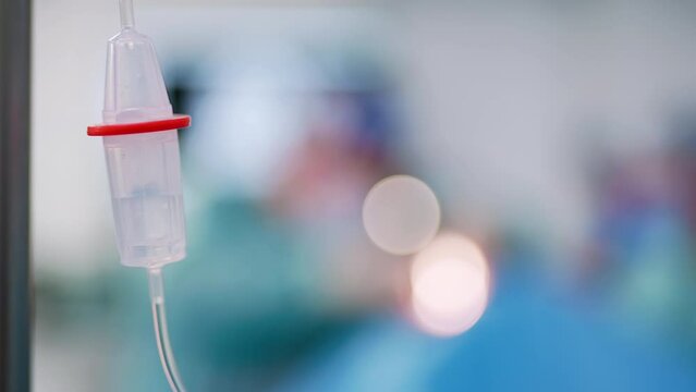Saline solution in the iv drip. Close up. Blurred backdrop with surgery in progress.
