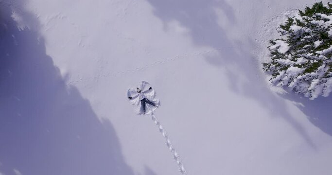 Aerial - Young woman making snow angel in a forest field