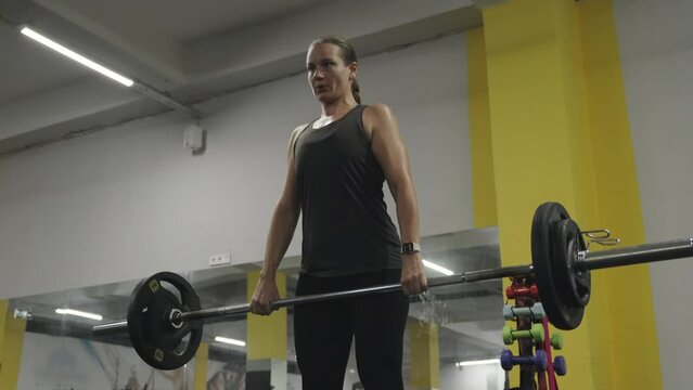 Camera Follows the Movements of a Young Woman Performing Romanian Deadlifts with a Barbell in the Gym!