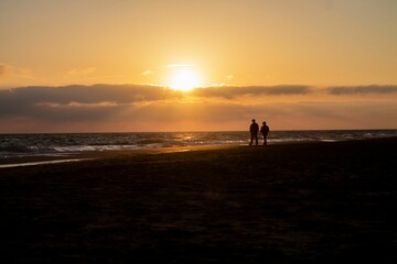 Silhouette view of a couple walking on the beach by the sea under orange sunset scene