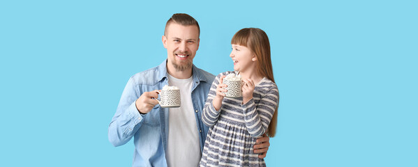 Happy daughter and father with cups of hot cocoa on blue background