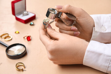 Female jeweler examining ring on beige table, closeup