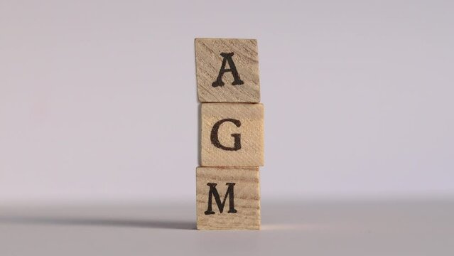 Letters spelling AGM are stacked on top of each other by a hand