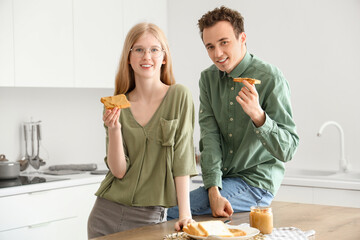 Happy young couple with tasty toasts of nut butter in kitchen