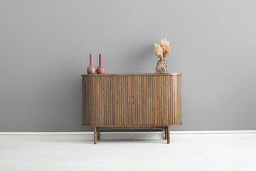 Wooden chest of drawers with pampas grass and decor near grey wall in room