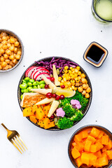 Vegan buddha bowl with sweet potato, quinoa, chickpeas, soybeans edamame, tofu, corn, cabbage, radish, broccoli and sesame seeds, white table background, top view. Autumn or winter healthy  slow food