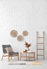 Light wooden coffee table with armchair and ladder near white brick wall