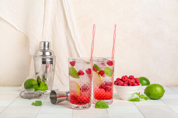 Glasses of fresh raspberry mojito and bowl with berries on white tile table