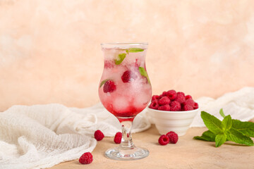 Glass of fresh raspberry mojito and bowl with berries on pink background
