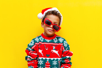 tired african american boy in christmas sweater and santa hat and crooked glasses on yellow...