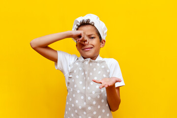 african american boy in uniform and chef's hat covers his nose with his hand and avoids the bad smell - obrazy, fototapety, plakaty