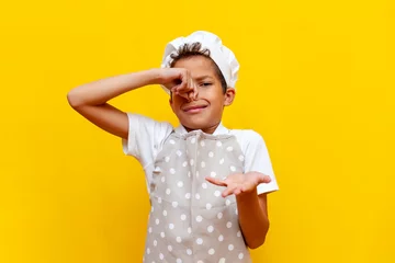 Foto op Canvas african american boy in uniform and chef's hat covers his nose with his hand and avoids the bad smell © Богдан Маліцький