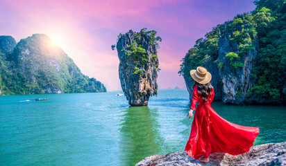 Female tourist in red dress looks at famous spot, James Bond Island, Thailand