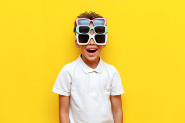 shocked african american boy with three sunglasses showing surprise on yellow isolated background - obrazy, fototapety, plakaty