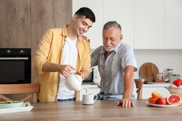 Young man pouring hot tea for his father in kitchen