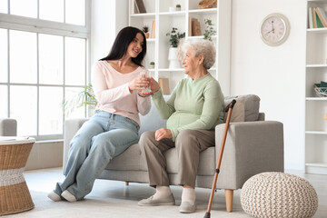 Obraz premium Senior woman taking glass of water from her daughter at home