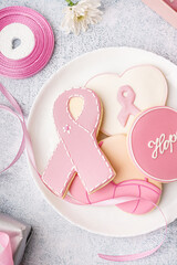 Plate with pink cookies in shape of ribbon on grey grunge background. Breast cancer awareness concept