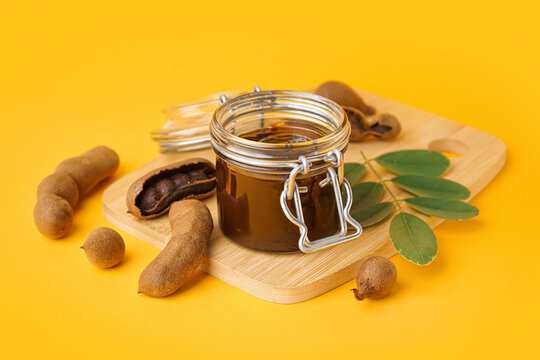 Jar with tasty tamarind jam with fruits on orange background