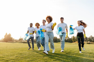 multiracial group of people running to clean the park from garbage and plastic with gloves and garbage bags - obrazy, fototapety, plakaty