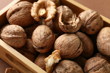 Wooden box of tasty walnuts on brown background, closeup