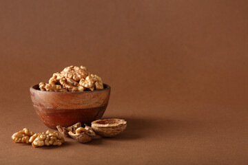 Bowl of tasty walnuts on brown background