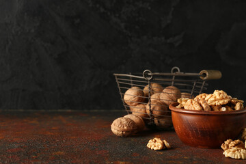 Bowl and basket of tasty walnuts on table against black wall