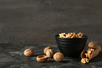 Bowl and scoop of tasty walnuts on table against grey wall