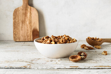 Bowl of tasty walnuts on table against white wall