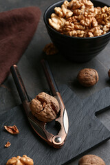 Nutcracker and bowl of tasty walnuts on grey background