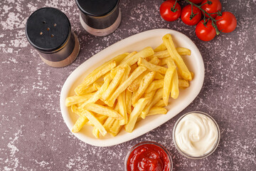 Plate of tasty french fries and sauces on grey background