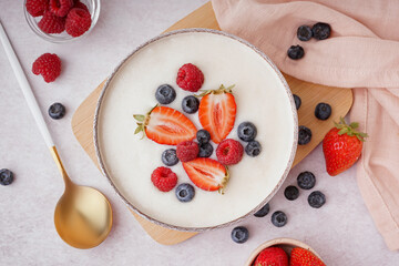 Bowl of tasty semolina porridge with fresh berries on white background