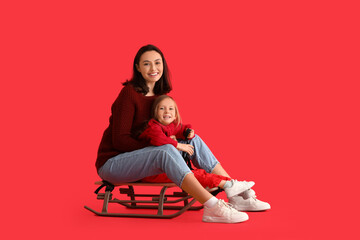 Obraz na płótnie Canvas Young mother and her little daughter with sled on red background