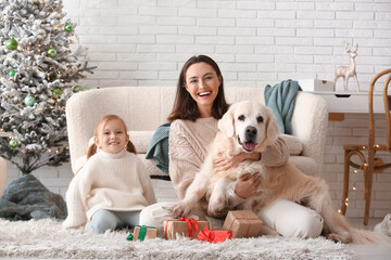 Happy young mother and her little daughter with cute Labrador dog at home on Christmas eve