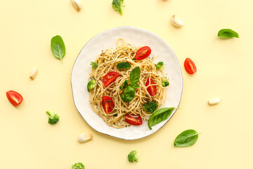 Plate of tasty pasta with broccoli and tomatoes on yellow background