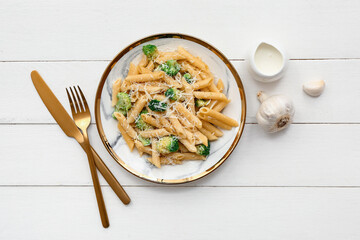 Plate of tasty pasta with broccoli on white wooden background