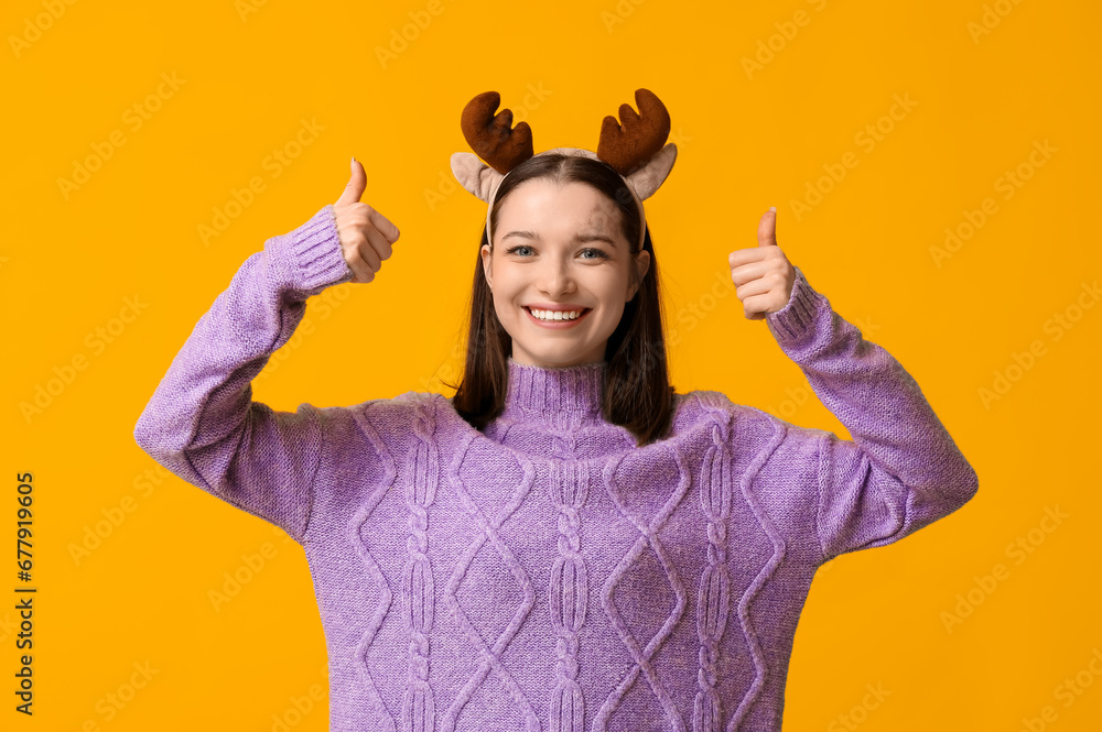 Canvas Prints beautiful young woman in reindeer horns showing thumbs-up on yellow background