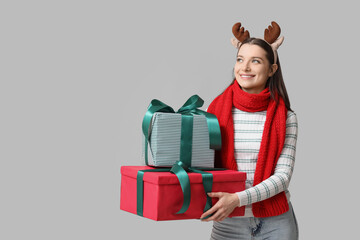Beautiful young woman in reindeer horns with gift boxes on grey background