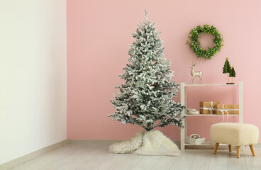 Beautiful Christmas tree with shelves and ottoman near pink wall