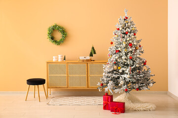 Beautiful Christmas tree with gift boxes and chest of drawers near beige wall
