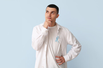 Handsome thoughtful man with blue ribbon on color background. Prostate cancer concept